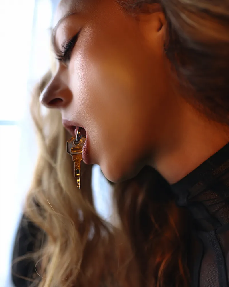 A gold key held between Goddess Nikki Kit's lips